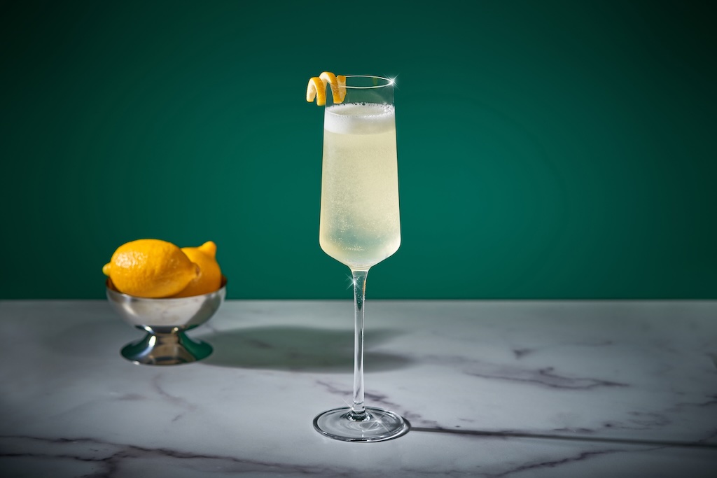 French 75 cocktail serveret i et slankt champagneglas med citronskal – en klassisk og elegant drink med gin, champagne, citron og sukker.