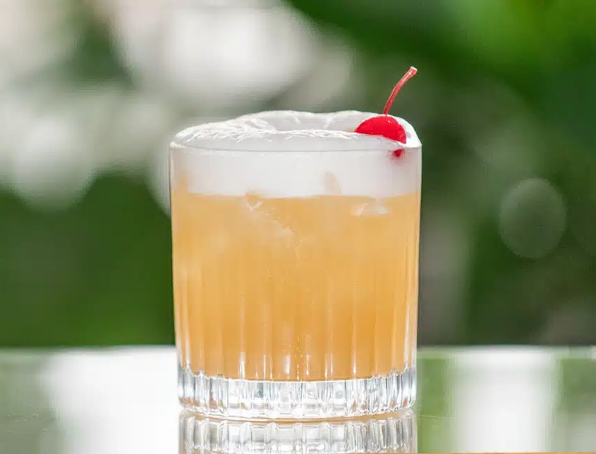 Amaretto Sour cocktail serveret med isterninger i et lowball-glas, pyntet med cocktailbær og skive citron – en sød og syrlig drink med italiensk mandellikør.