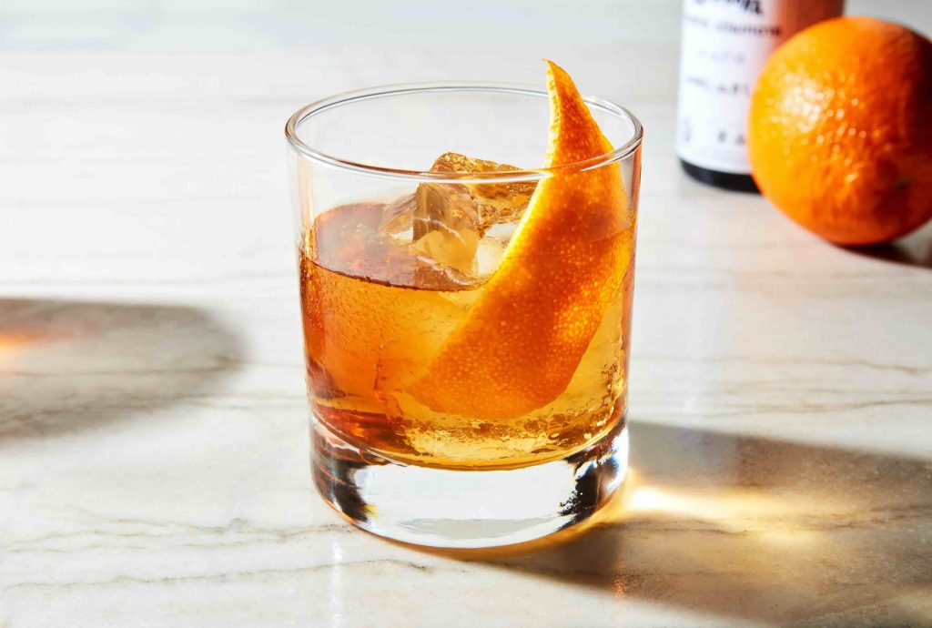 Apple Pie Old Fashioned – klassisk cocktail med æbletærte-twist, serveret i et lavt glas med isterninger, kanelstang og æbleskive som pynt.