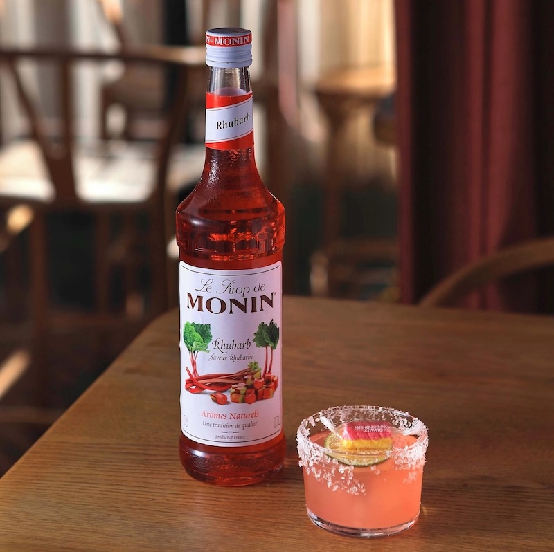 Rabarber Margarita i saltet glas med rosa nuance, isterninger og lime – en frisk og syrlig cocktail med sommerstemning.