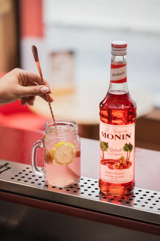 Rabarber-lemonade serveret i højt glas med isterninger og skive citron – en forfriskende sommerdrink med lyserød farve og naturlig syrlighed.