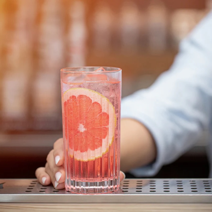 Rhubarb Paloma cocktail i lavt glas med isterninger, pyntet med tørret citrus og frisk rabarber – en frisk, lyserød drink med sommerlig udtryk.